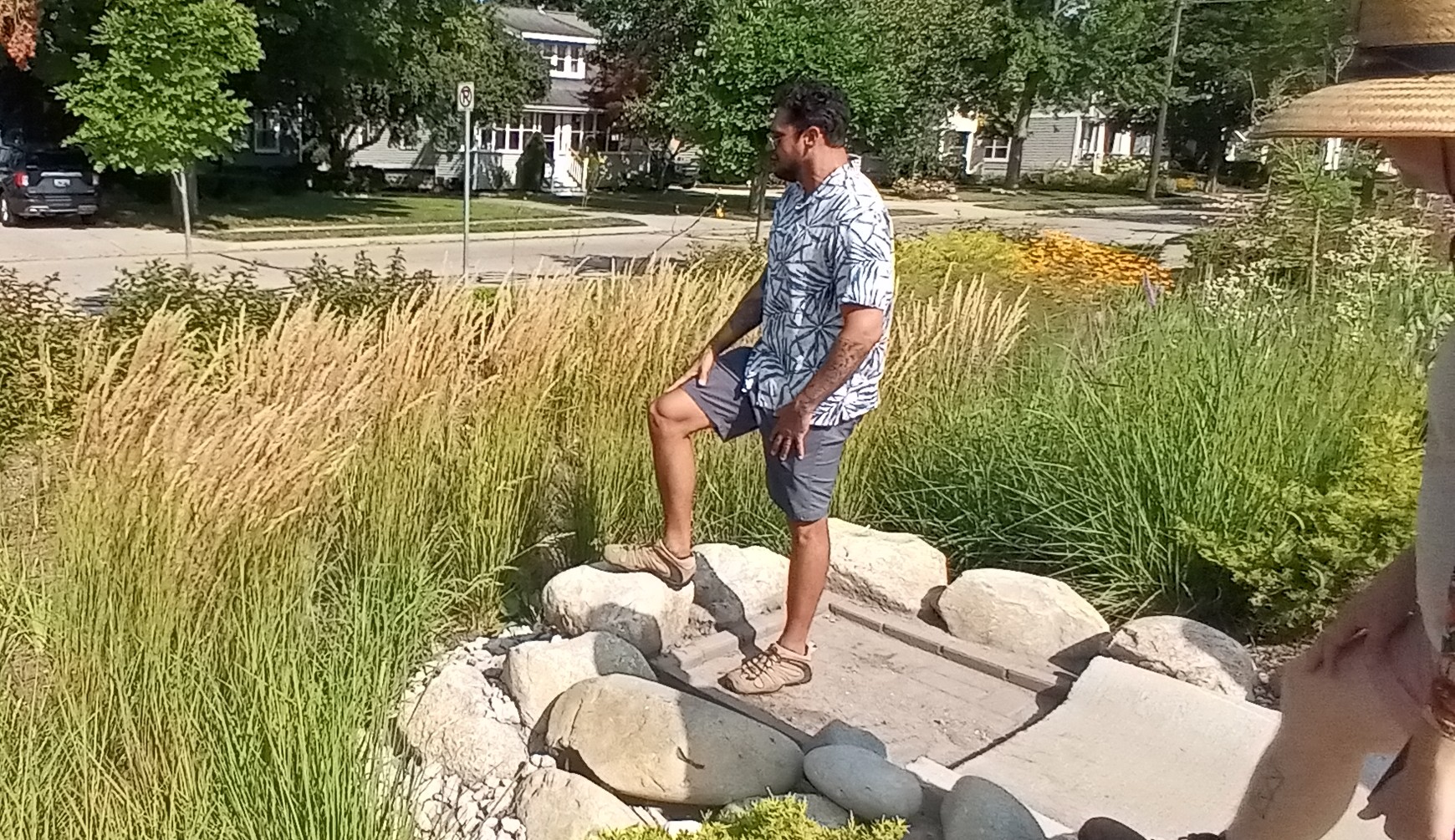 A person standing amongst rocks in a rain garden located next to a parking lot and houses.